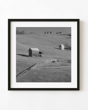 Wooden sheds and haystacks across rolling Romanian farmland in black and white