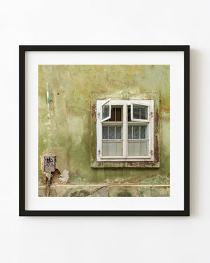 Open white window on a weathered green wall in Romania