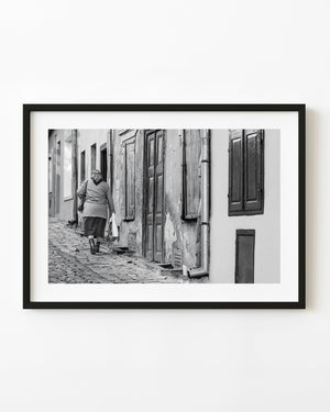Woman walking along a Romanian cobblestone lane in black and white