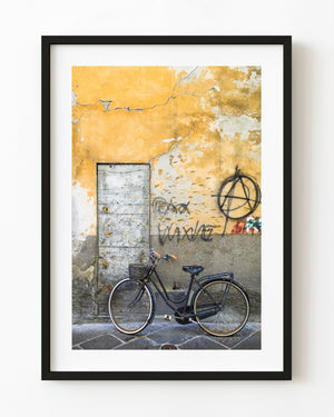 Black bicycle with a basket against an ochre graffiti-covered wall in Rome