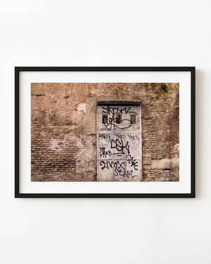Graffiti-covered pale door set into a weathered wall in Rome