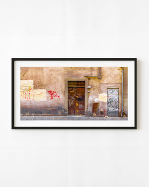 Graffiti-covered metal doors on a warm plaster wall in Rome