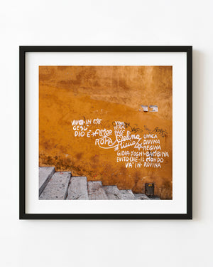 White graffiti on an orange Roman wall above stone steps