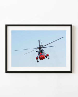 Royal Navy Sea King helicopter banking against a pale blue sky