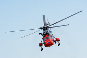 Colour aviation photograph of a red and grey Sea King in flight