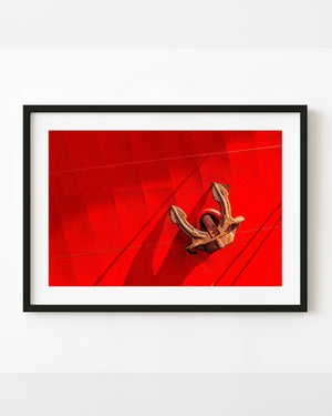 Rusted anchor hanging against a vivid red commercial ship hull