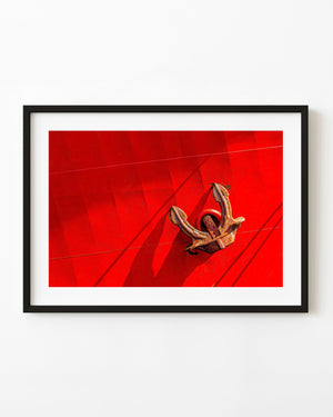 Rusted anchor hanging against a vivid red commercial ship hull
