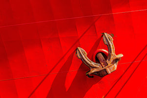 Rusted ship anchor against a bright red painted hull