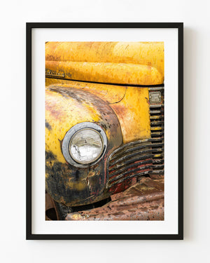 Round headlight and curved grille on a rusted yellow vintage truck