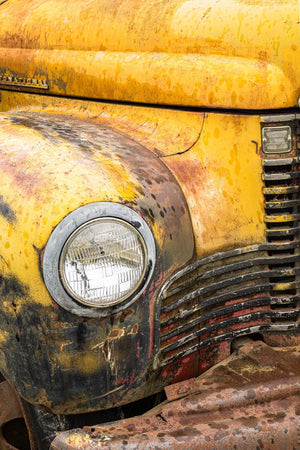 Colour close-up of a weathered yellow truck with peeling paint and a chrome headlight rim