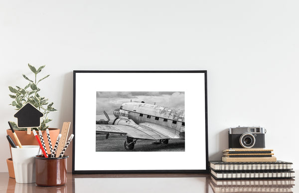 Grounded military aircraft with peeling paint and overgrown field in black and white