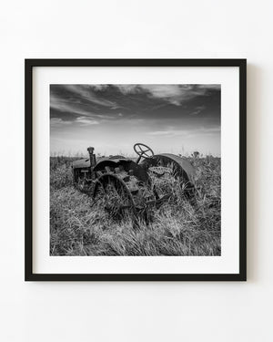 Rusting prairie tractor surrounded by tall grass in black and white