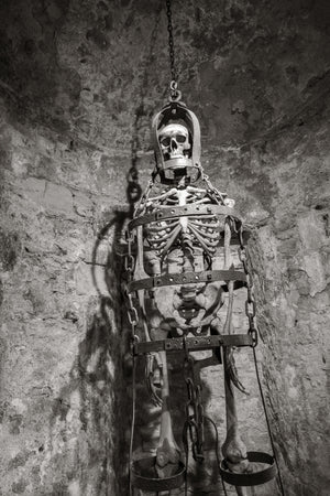 Skeleton exhibit held in an iron cage against a Rye Castle stone wall