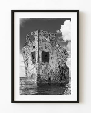 Black and white SS Sapona shipwreck hull rising above the sea beneath bright clouds.