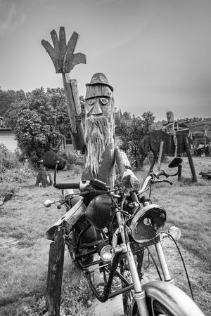 Carved wooden figure raising a hand behind a weathered motorcycle