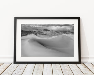Bright dune ridges contrasting with rocky mountains and dark clouds