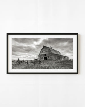 Abandoned Saskatchewan barn beneath storm clouds in black and white