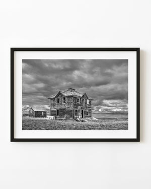 Abandoned Saskatchewan farmhouse beneath heavy clouds in black and white