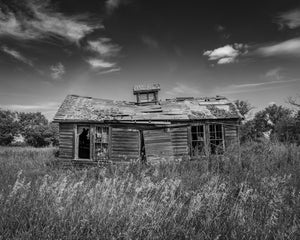 Deteriorating wooden farmhouse with broken windows and a sagging roof