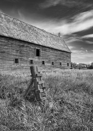 Weathered barn beside a tilted wooden fence post in tall grass