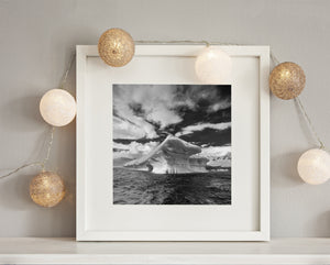 Monochrome polar seascape with a weathered iceberg beneath dramatic clouds