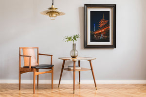 Wooden chair and table with a vase and framed picture in a room.