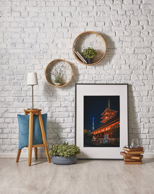 Decorative interior setting with framed picture, plants, and small table against a white brick wall.