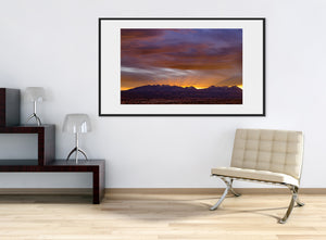 Purple sunset clouds sweep above dark Sierra peaks and low desert vegetation.