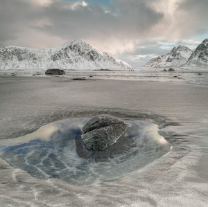 Snow-covered mountains beyond a shallow pool and foreground rock