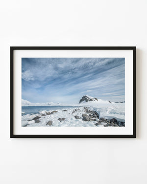 Snowy Antarctic shore beneath streaked blue skies