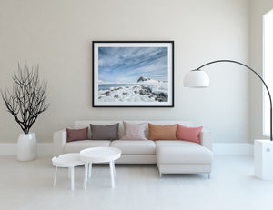 Snowy coastal headland beneath a broad pale blue sky