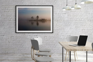 Warm dawn light filtering through fog above calm reflective water