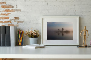 Tree silhouettes reflected in still water beside a misty lakeside house