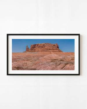 Red desert butte above pale eroded badlands beneath a blue sky.
