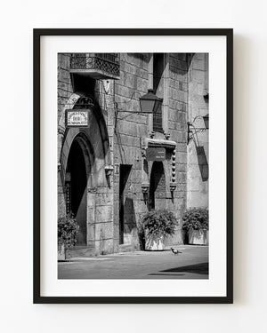 Black and white Spanish stone facade with arched doorway, iron balcony and hanging lantern.