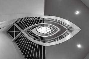 Curving museum stair rails frame an eye-shaped skylight in monochrome.