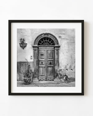 Black and white Spoleto wooden double door beneath a stone arch and fan-shaped grille.