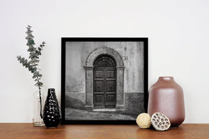 Square monochrome photograph of an aged Italian door and textured wall.
