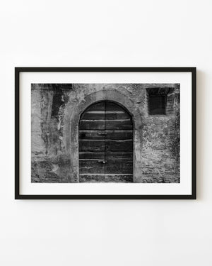 Weathered arched wooden double door in a rough Spoleto wall, photographed in black and white.