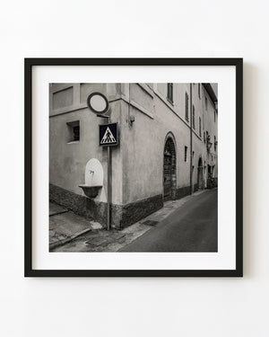 Spoleto street corner with a wall fountain, road signs and arched doors in toned monochrome.