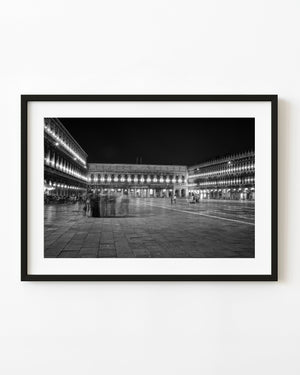 St Marks Square in Venice at night with illuminated arcades and blurred visitors in black and white.