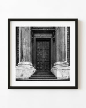Black and white St Pauls Cathedral entrance with fluted stone columns and dark paneled doors.