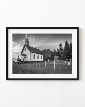 Black and white St Sylvesters Church in Ontario beside a cemetery and evergreen woodland.