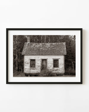 Weathered cabin at St Sylvesters Mission Church, with boarded windows and a worn shingle roof in monochrome.