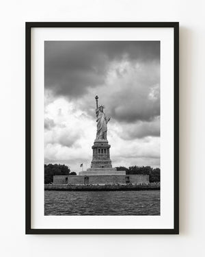 Statue of Liberty and Liberty Island beneath dramatic clouds in black and white.