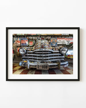Sticker-covered Pontiac front surrounded by vintage signs in a Route 66 shop.
