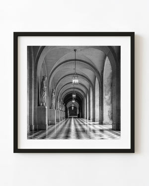 Black and white stone corridor with repeating arches, statues and a checkered floor.