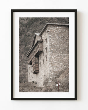 Tall stone building with projecting wooden window bays beneath a wooded hillside in China.