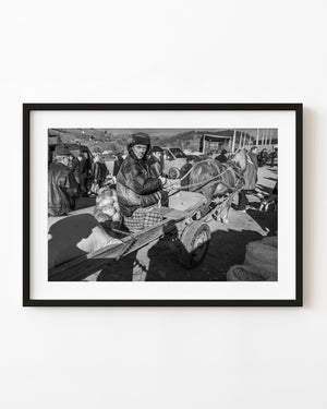 Suceava farmer seated on a horse-drawn wagon at a busy rural market in black and white.