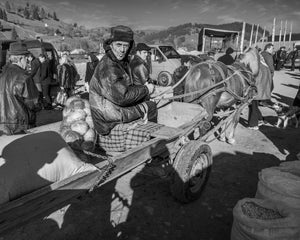 Romanian farmer holds reins beside sacks on a wooden wagon.